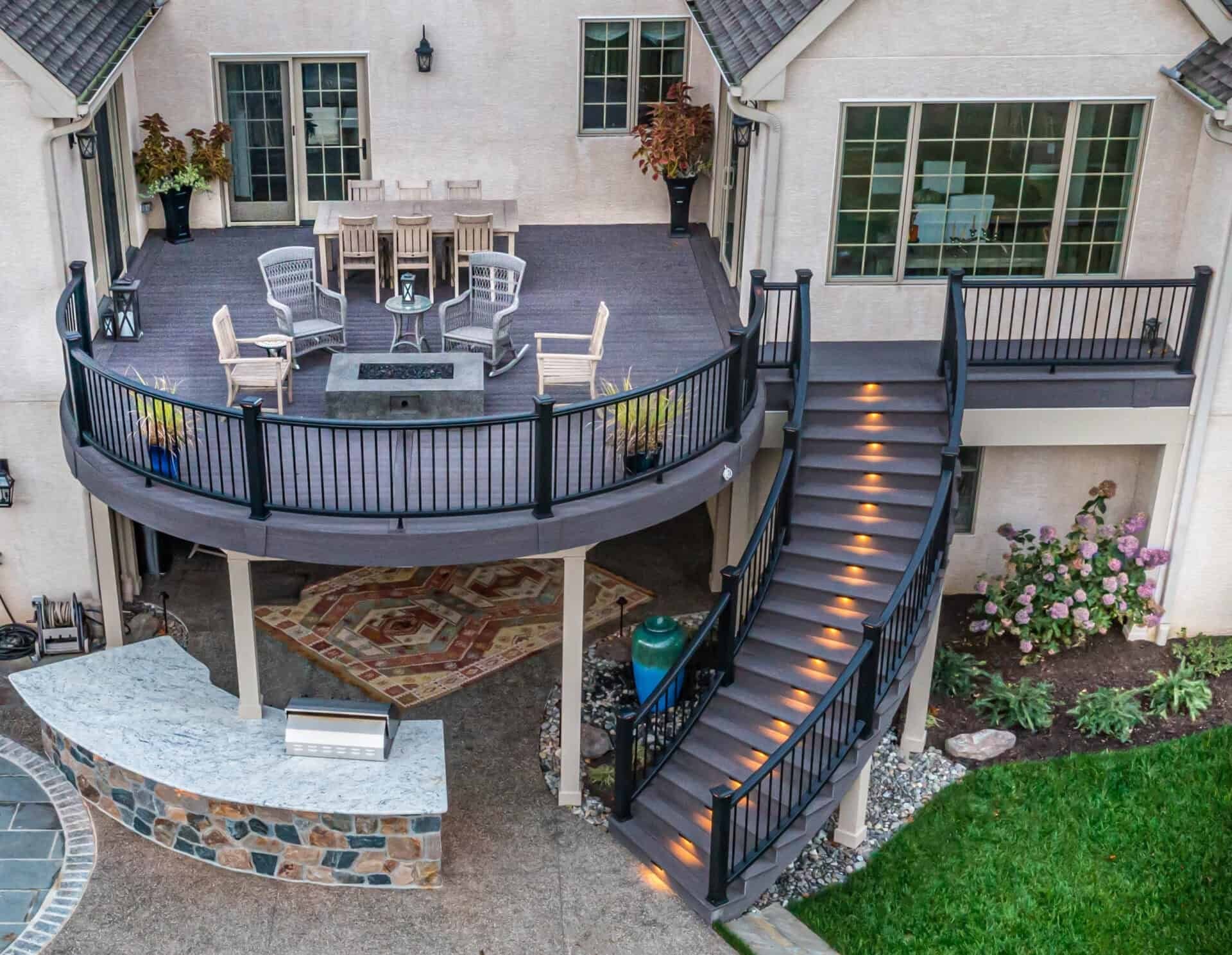 Elevated custom deck with a curved lounge area, black railings, illuminated stairs, and a covered patio below