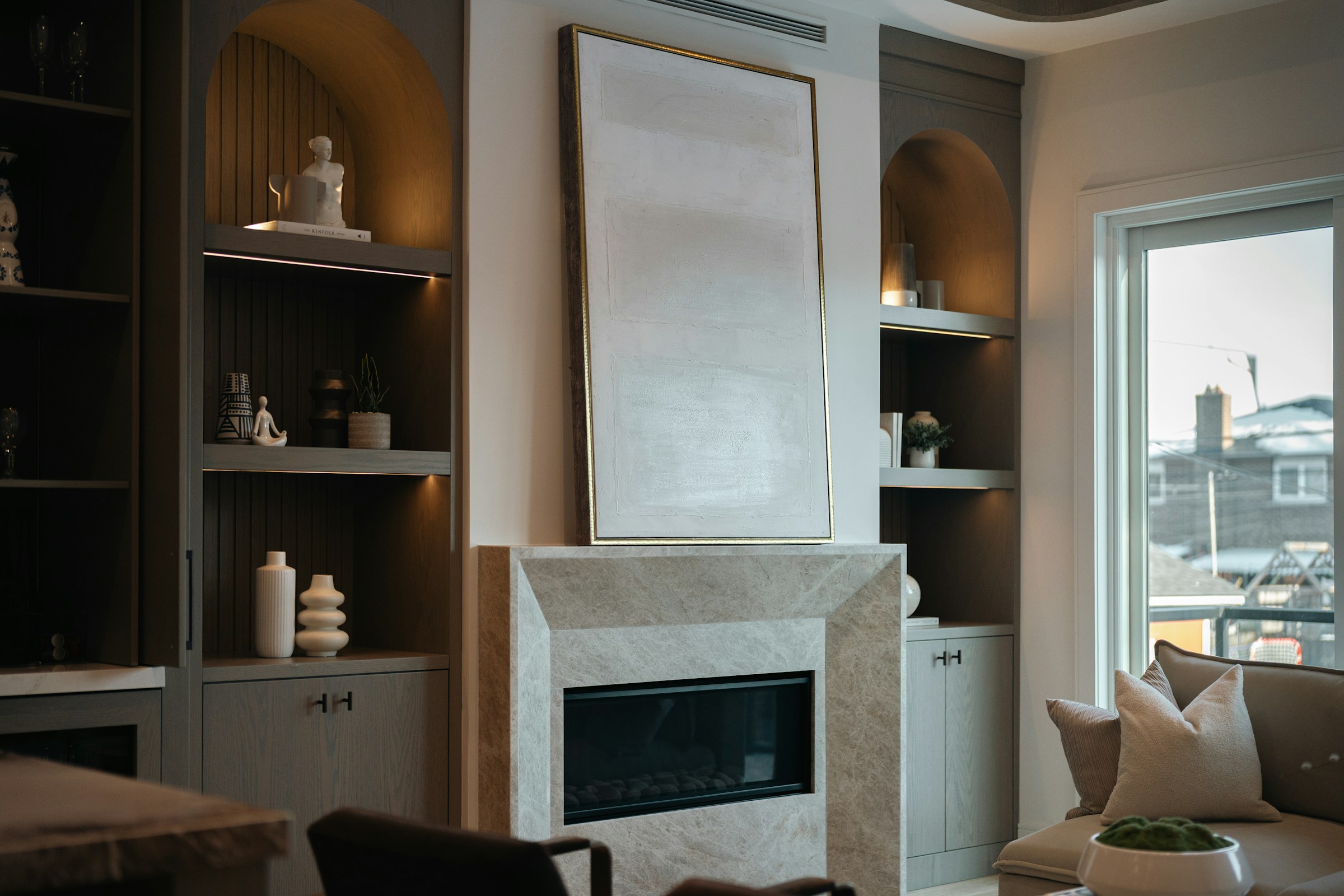 High-resolution real photograph of luxury arched built-ins with integrated lighting, ribbed wood backing, fitted cabinets, and a stone fireplace