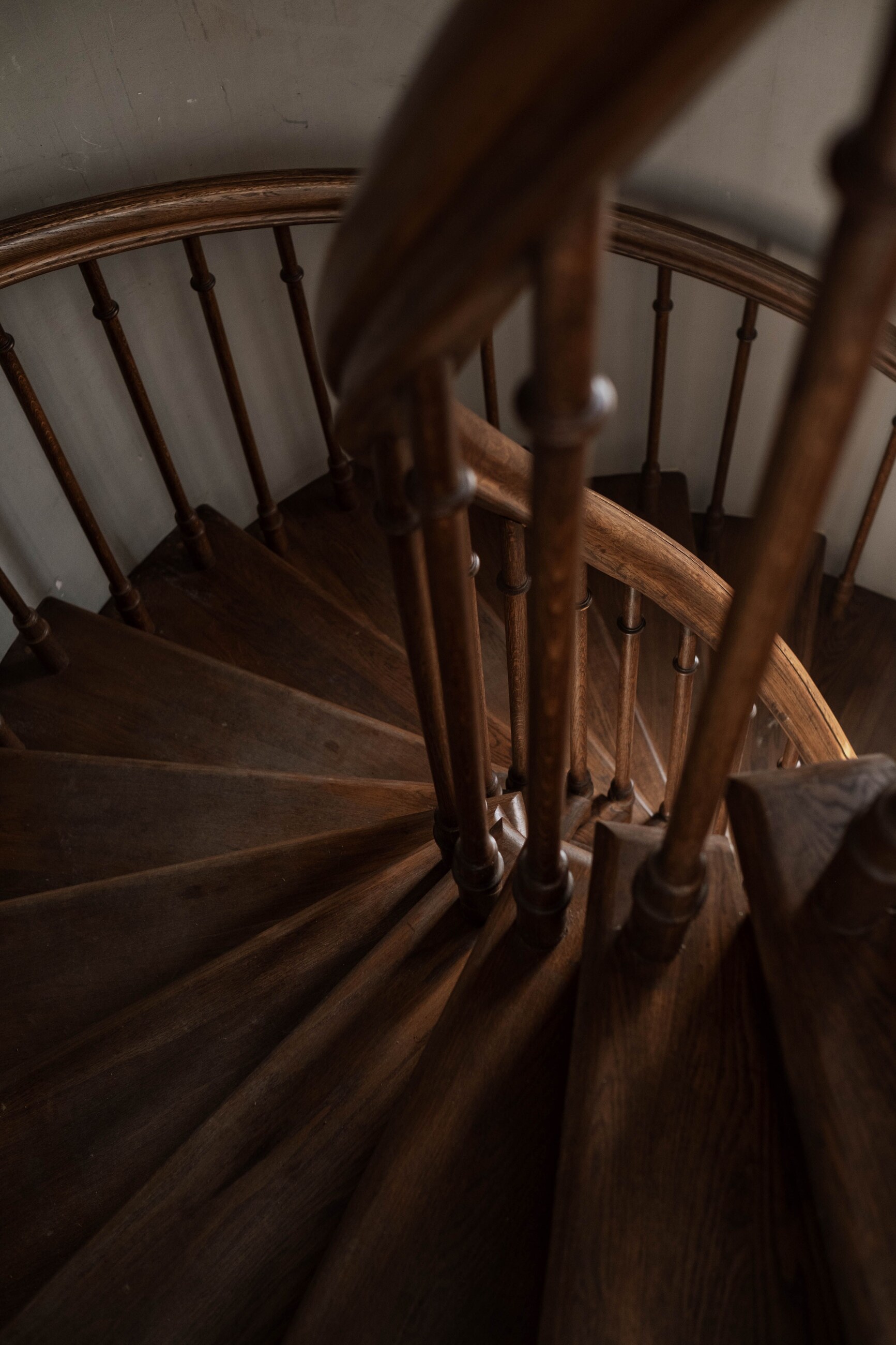 High-resolution real photograph of a curved solid-wood staircase with detailed balusters and newel